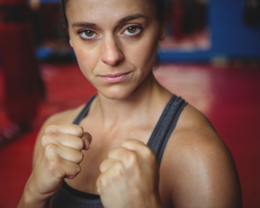 Portrait of confident female boxer performing boxing stance in fitness studio